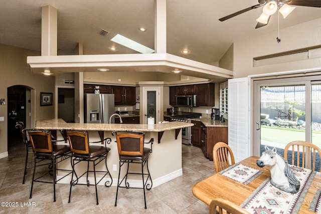 kitchen featuring vaulted ceiling, a breakfast bar area, ceiling fan, dark brown cabinetry, and stainless steel appliances