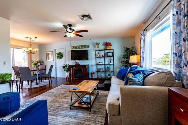 living area with visible vents, dark wood finished floors, a fireplace, and ceiling fan with notable chandelier