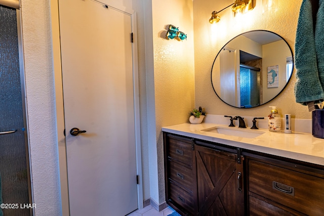 full bathroom with a shower with shower door, a textured wall, and vanity