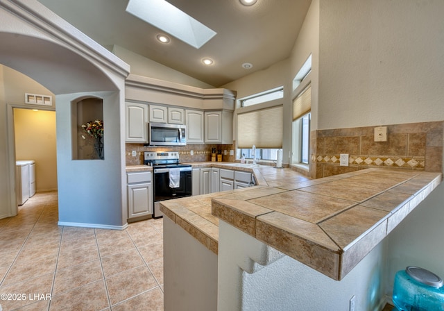 3000 Mirage Dr, Lake Havasu City, AZ 86404 - kitchen with appliances with stainless steel finishes, a peninsula, decorative backsplash, lofted ceiling, and a skylight