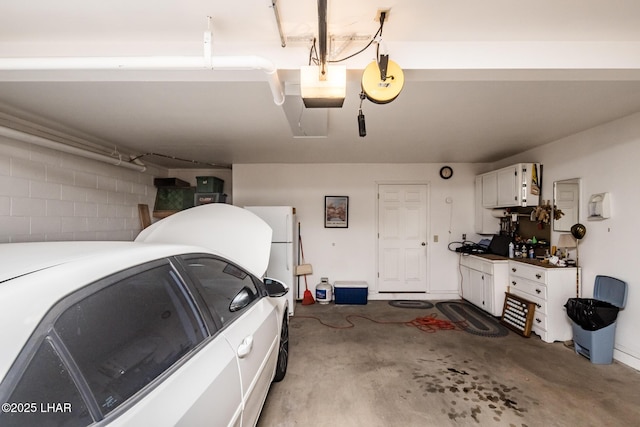 garage featuring concrete block wall, a garage door opener, and freestanding refrigerator