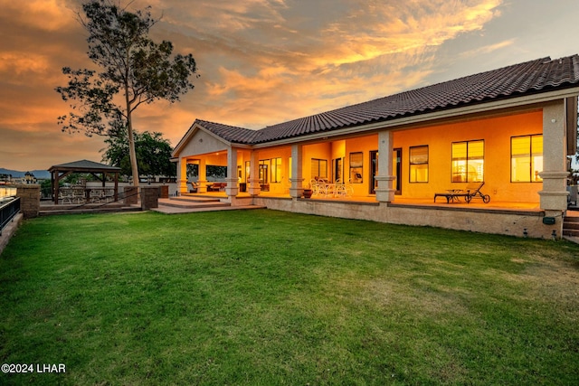 back house at dusk featuring a gazebo and a lawn