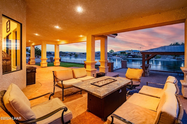 patio terrace at dusk featuring a gazebo, an outdoor living space with a fire pit, and a water view