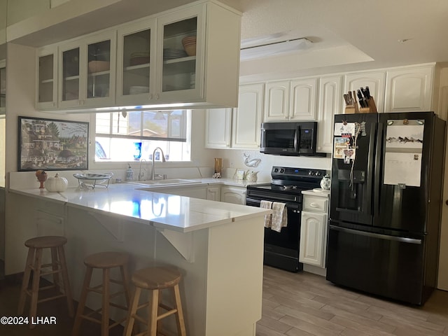 kitchen with black appliances, kitchen peninsula, white cabinets, and a breakfast bar