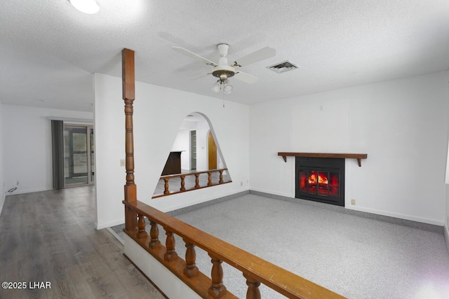 unfurnished living room featuring visible vents, a textured ceiling, a glass covered fireplace, baseboards, and ceiling fan