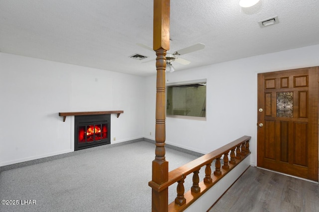 entryway featuring baseboards, visible vents, ceiling fan, a textured ceiling, and a glass covered fireplace