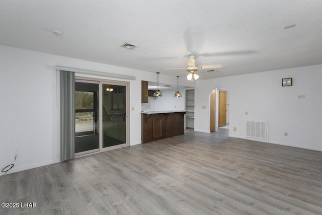 unfurnished living room featuring visible vents, arched walkways, a textured ceiling, and a ceiling fan