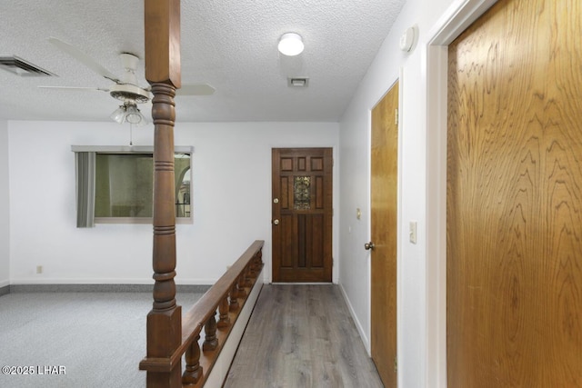 hall featuring baseboards, visible vents, and a textured ceiling