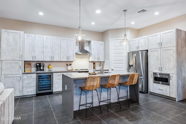 kitchen featuring appliances with stainless steel finishes, sink, beverage cooler, a kitchen island with sink, and wall chimney range hood