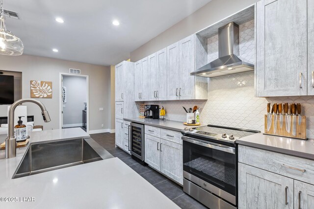 kitchen with pendant lighting, sink, wine cooler, stainless steel electric stove, and wall chimney exhaust hood