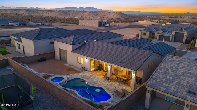 pool at dusk with an in ground hot tub, a mountain view, an outdoor bar, and a patio