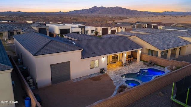 back house at dusk with an in ground hot tub, a mountain view, and a patio area