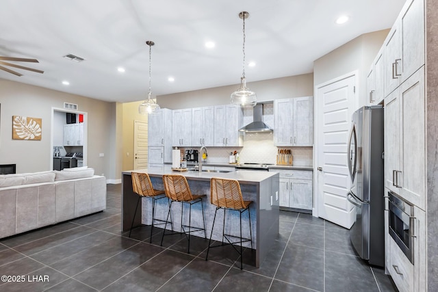 kitchen with sink, wall chimney range hood, stainless steel appliances, a kitchen island with sink, and white cabinets