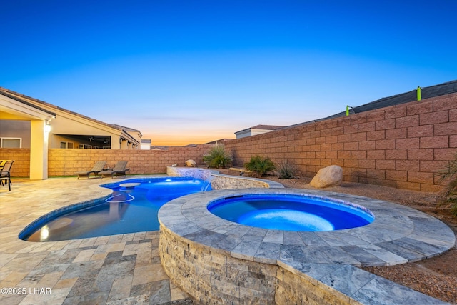 pool at dusk featuring an in ground hot tub, pool water feature, and a patio