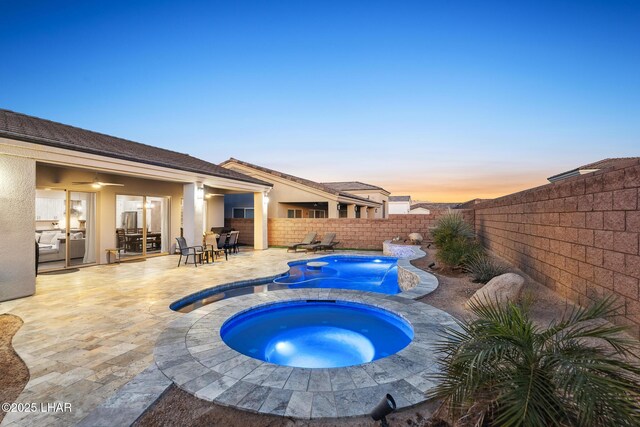 pool at dusk featuring an in ground hot tub, pool water feature, and a patio area