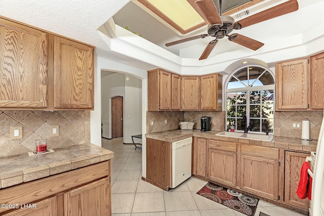 kitchen with sink, tile countertops, light tile patterned floors, a tray ceiling, and white dishwasher