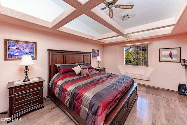 bedroom featuring beamed ceiling, light wood-type flooring, coffered ceiling, ceiling fan, and a textured ceiling