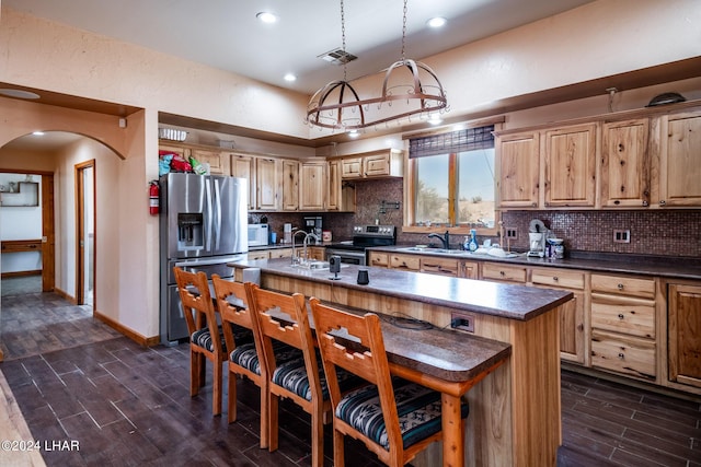 kitchen with hanging light fixtures, appliances with stainless steel finishes, a center island with sink, and backsplash