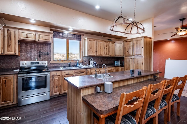 kitchen featuring tasteful backsplash, sink, stainless steel range with electric stovetop, hanging light fixtures, and a kitchen island with sink