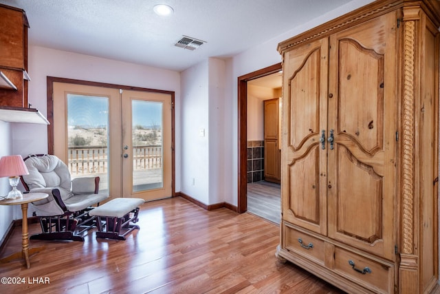 sitting room featuring light hardwood / wood-style flooring, a textured ceiling, and french doors