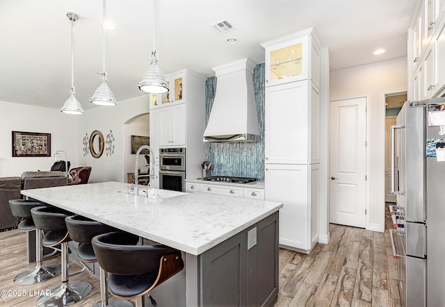 2800 Papeete Dr, Lake Havasu City, AZ 86404 - kitchen with custom exhaust hood, tasteful backsplash, white cabinets, appliances with stainless steel finishes, and light wood finished floors