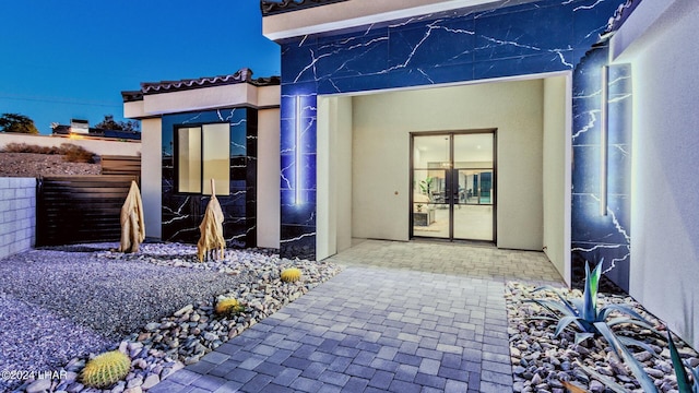 view of exterior entry with a patio, fence, and stucco siding