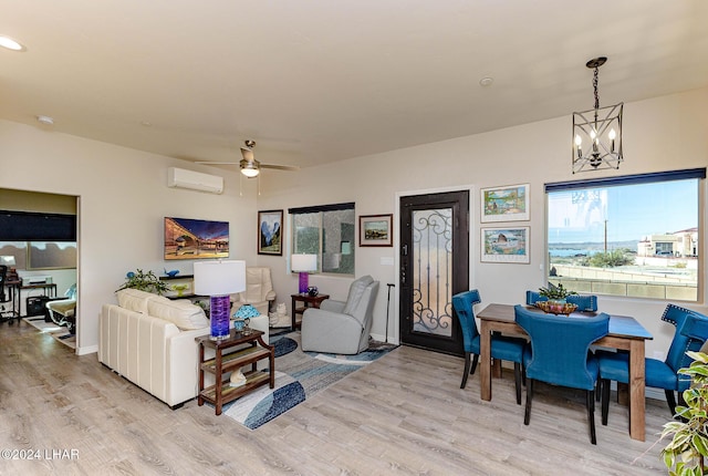 living room with a wall mounted AC, ceiling fan with notable chandelier, and light hardwood / wood-style flooring