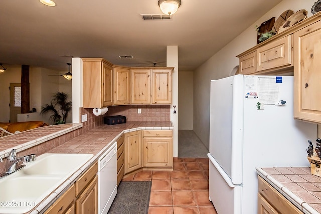 kitchen featuring tile counters, a sink, light brown cabinets, and white appliances