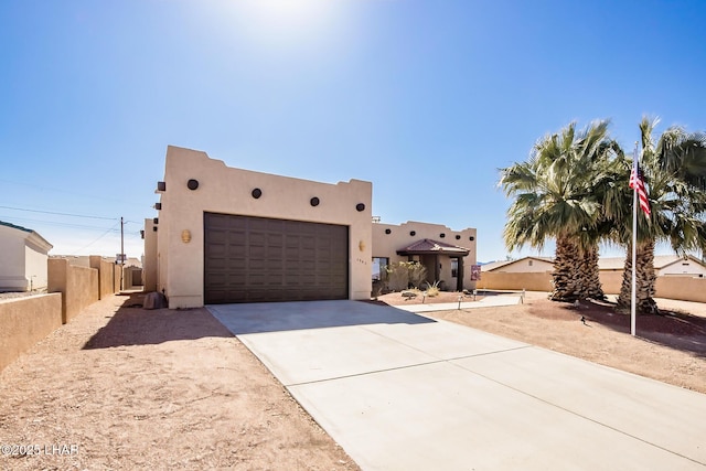 pueblo revival-style home featuring driveway, stucco siding, fence, and an attached garage
