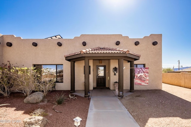 adobe home with stucco siding, fence, and a tile roof