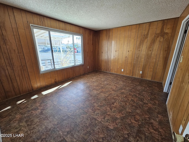 empty room featuring a textured ceiling and wood walls