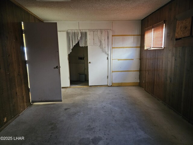 unfurnished room featuring a textured ceiling and wood walls