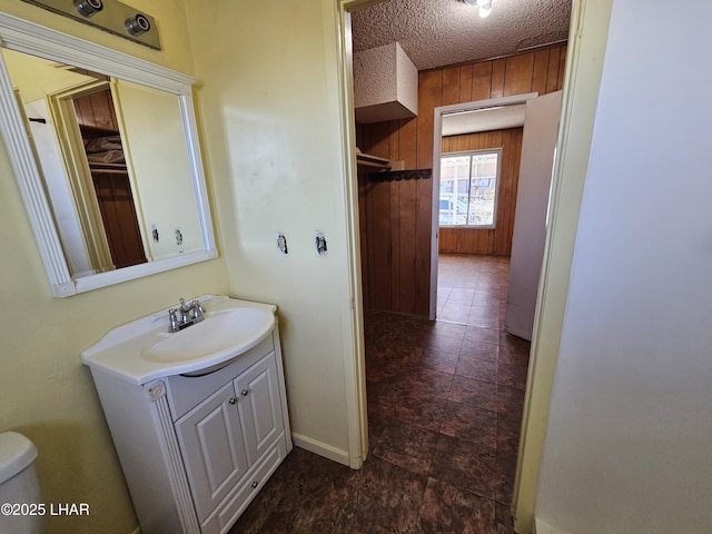 bathroom featuring vanity, toilet, a textured ceiling, and wood walls