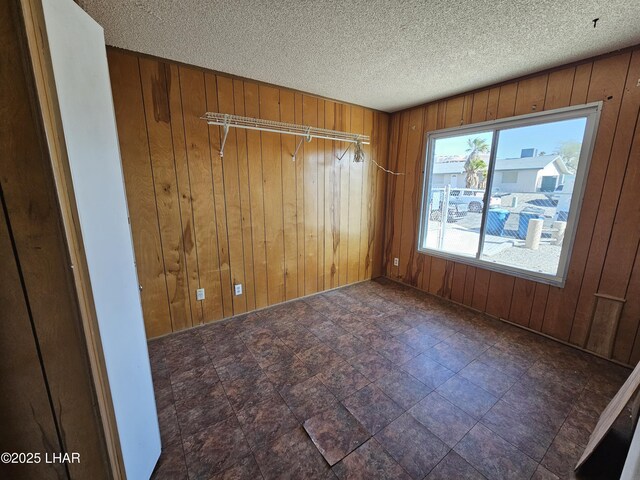 unfurnished room featuring a textured ceiling and wood walls