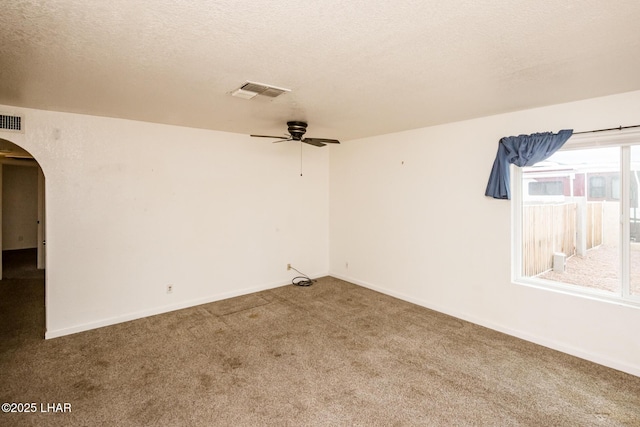 spare room featuring carpet flooring, visible vents, arched walkways, and a textured ceiling