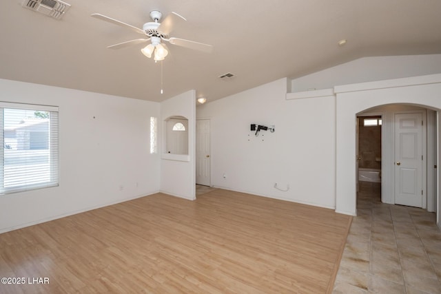 unfurnished living room with a ceiling fan, arched walkways, lofted ceiling, and visible vents