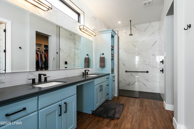 bathroom with a marble finish shower, visible vents, wood finished floors, and vanity