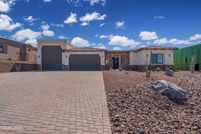 mediterranean / spanish home with an attached garage, stucco siding, stone siding, a tile roof, and decorative driveway