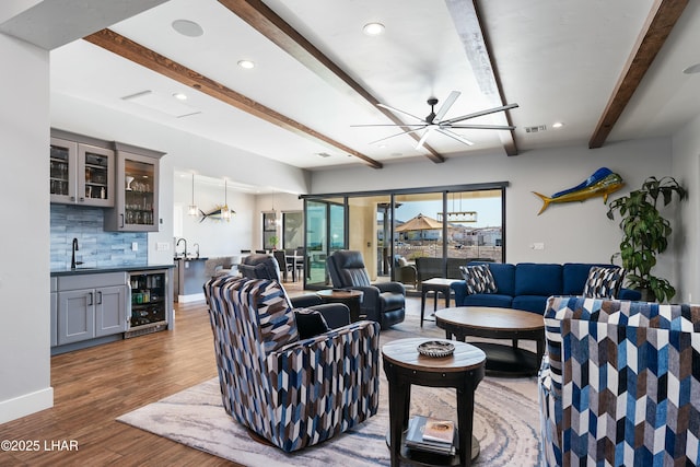 living room with wood finished floors, a ceiling fan, beverage cooler, beam ceiling, and indoor wet bar