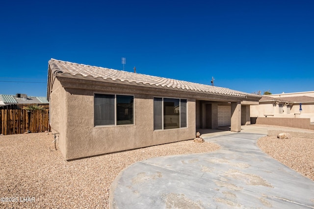 rear view of house with a garage, fence, driveway, a tiled roof, and stucco siding