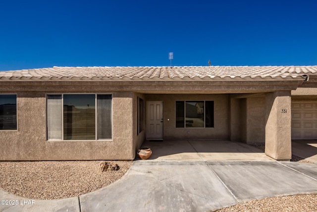 view of exterior entry with a tile roof, a patio, and stucco siding