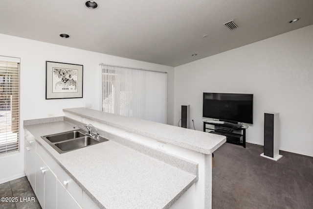 kitchen featuring light countertops, visible vents, white cabinetry, a sink, and a peninsula