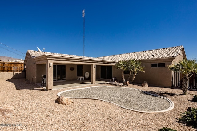 rear view of house featuring a tiled roof, a patio area, fence, and stucco siding