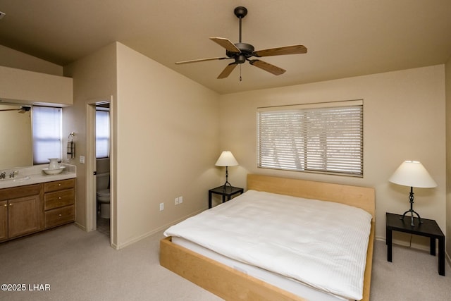 bedroom featuring vaulted ceiling, ensuite bathroom, a sink, and light colored carpet