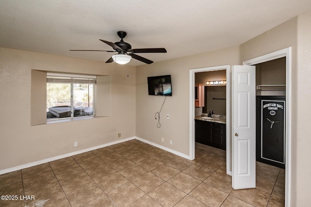 unfurnished bedroom featuring light tile patterned floors, baseboards, ceiling fan, a textured ceiling, and a sink