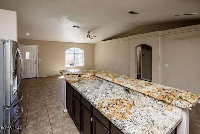 kitchen with arched walkways, lofted ceiling, visible vents, tile patterned floors, and stainless steel fridge