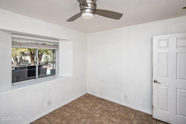 tiled empty room with ceiling fan, baseboards, and a textured ceiling