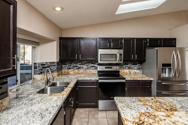 kitchen featuring light tile patterned floors, stainless steel appliances, lofted ceiling, tasteful backsplash, and a sink