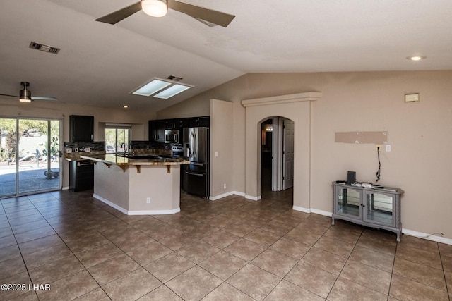 kitchen with arched walkways, ceiling fan, lofted ceiling, a breakfast bar, and appliances with stainless steel finishes