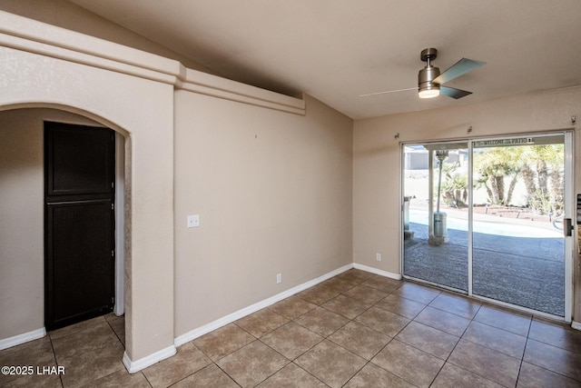 empty room featuring a ceiling fan, arched walkways, tile patterned flooring, and baseboards